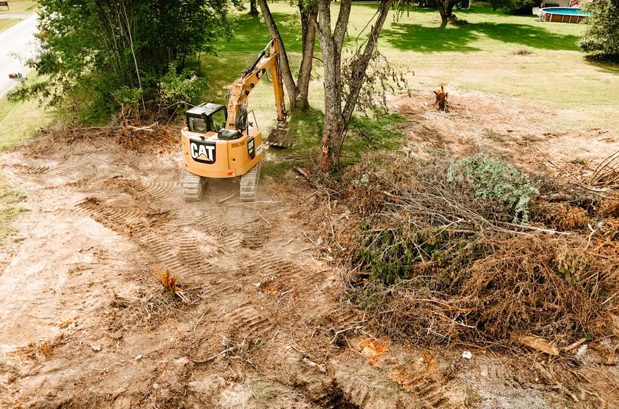 Elevated view of a CAT excavator clearing trees beside a large brush pile