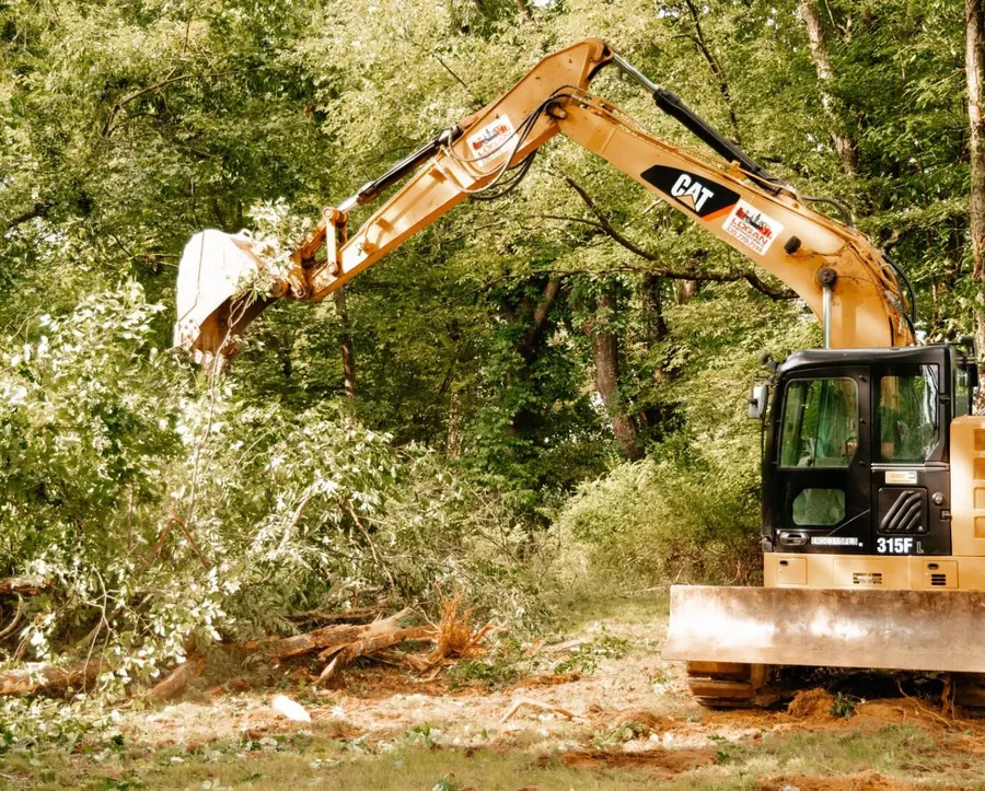 CAT excavator pulling brush and small trees from a wooded edge