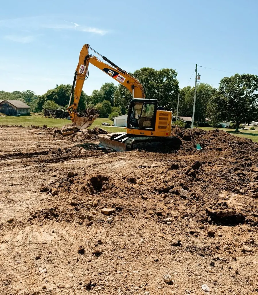 CAT excavator digging on a stripped dirt lot with houses in the distance