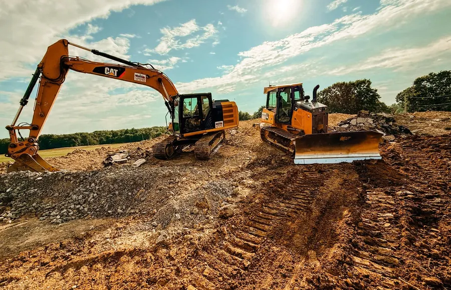 CAT excavator and a dozer working rough dirt and broken rock under a bright sky