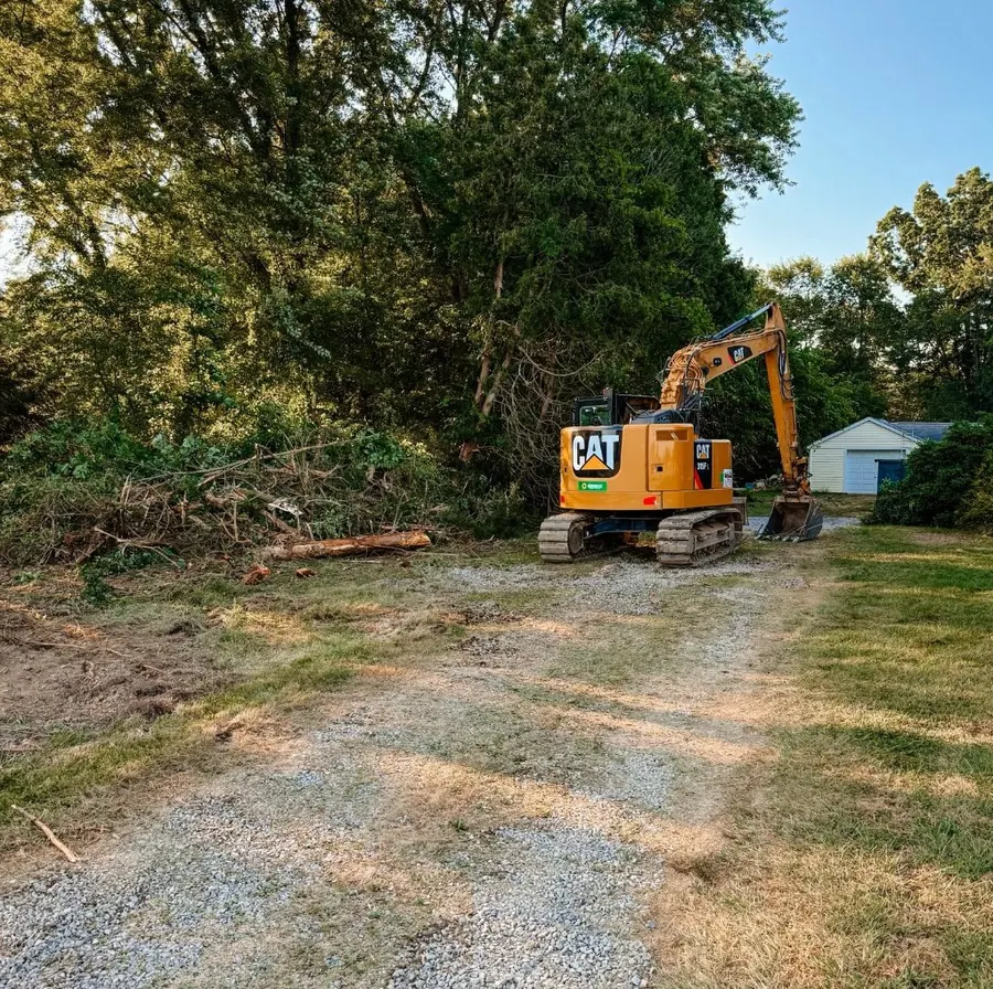 CAT excavator at the end of a gravel drive beside cleared brush