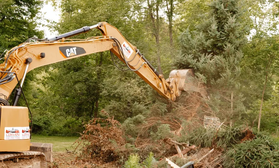 CAT excavator with a Logan Earthworks decal pushing over an evergreen tree