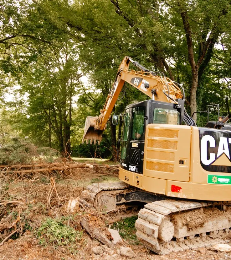 Rear view of a CAT excavator tearing out brush under trees