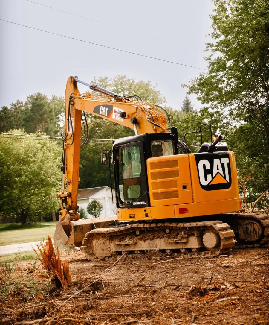CAT excavator parked on cleared ground beside a splintered stump