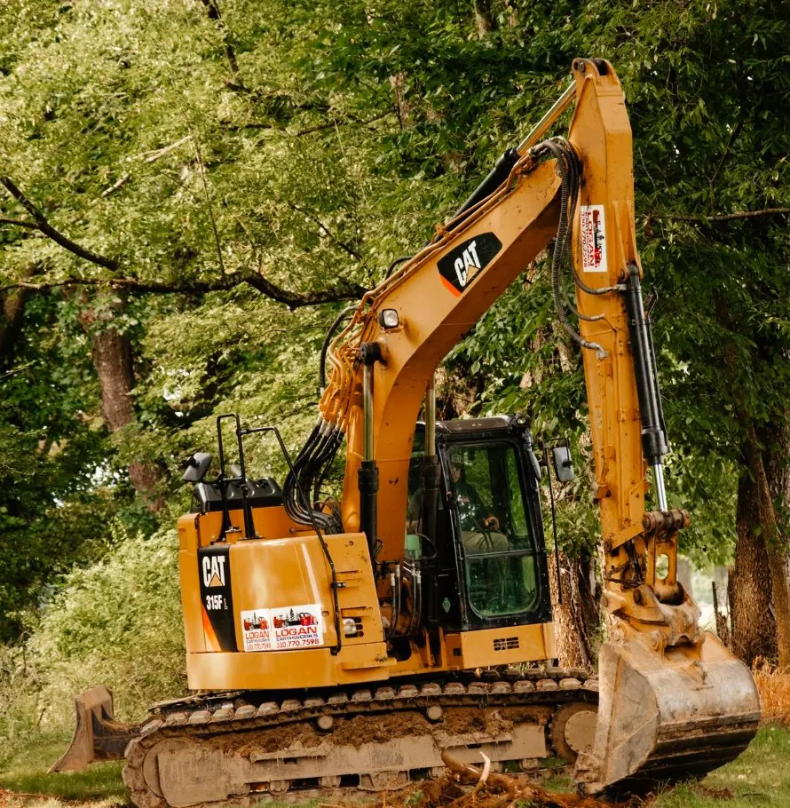 CAT excavator with Logan Earthworks decals parked under large shade trees