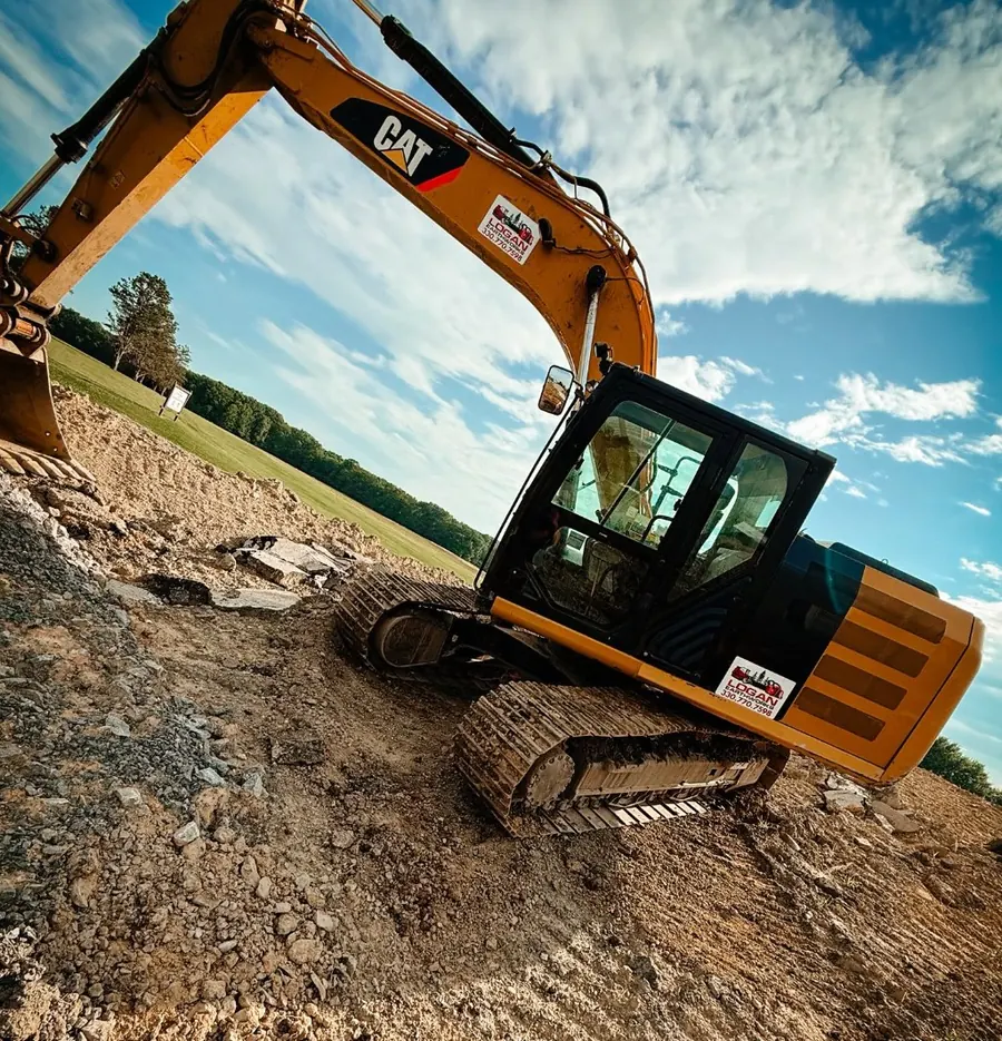 CAT excavator with Logan Earthworks decals on broken rock and dirt under a big sky