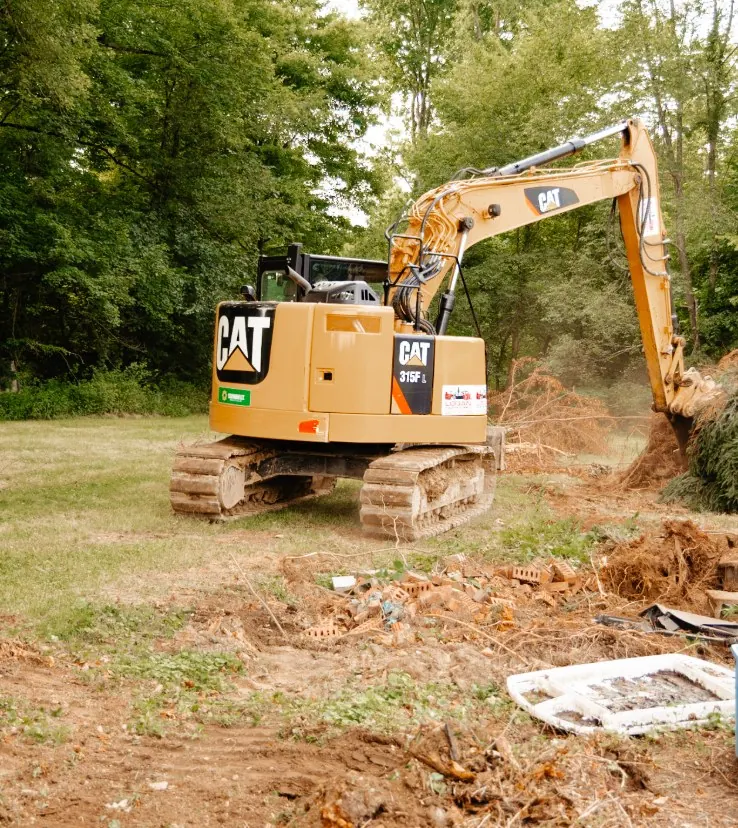 CAT excavator pulling out shrubs near scattered bricks and yard debris