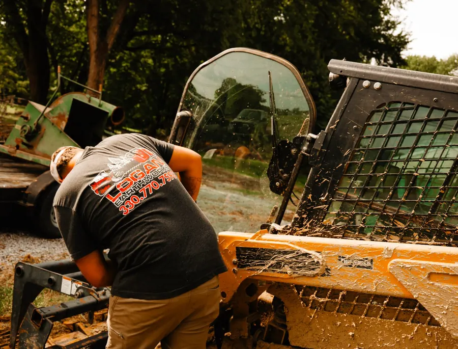 Crew member in a Logan Earthworks shirt working at the front of a muddy loader