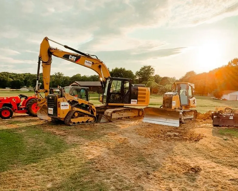 CAT excavator, compact track loader and dozer parked on a dirt pad at sunset