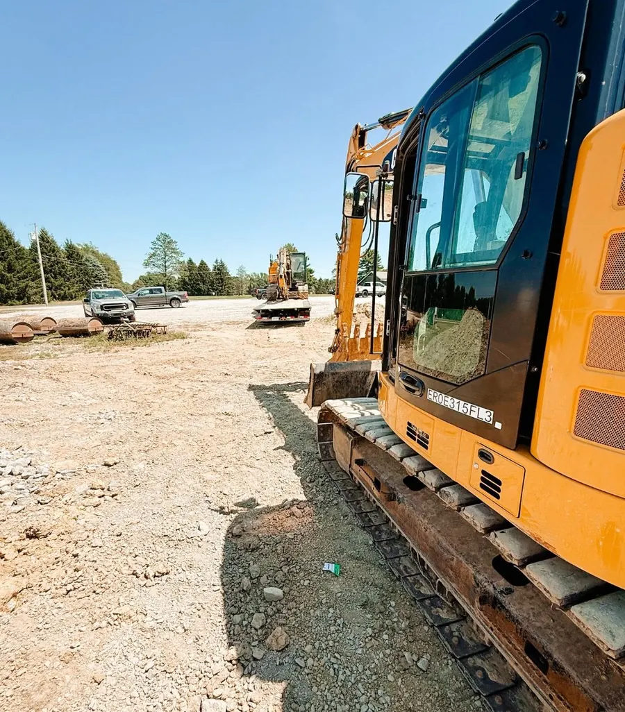 Side of an excavator on a crushed stone lot with trucks in the distance