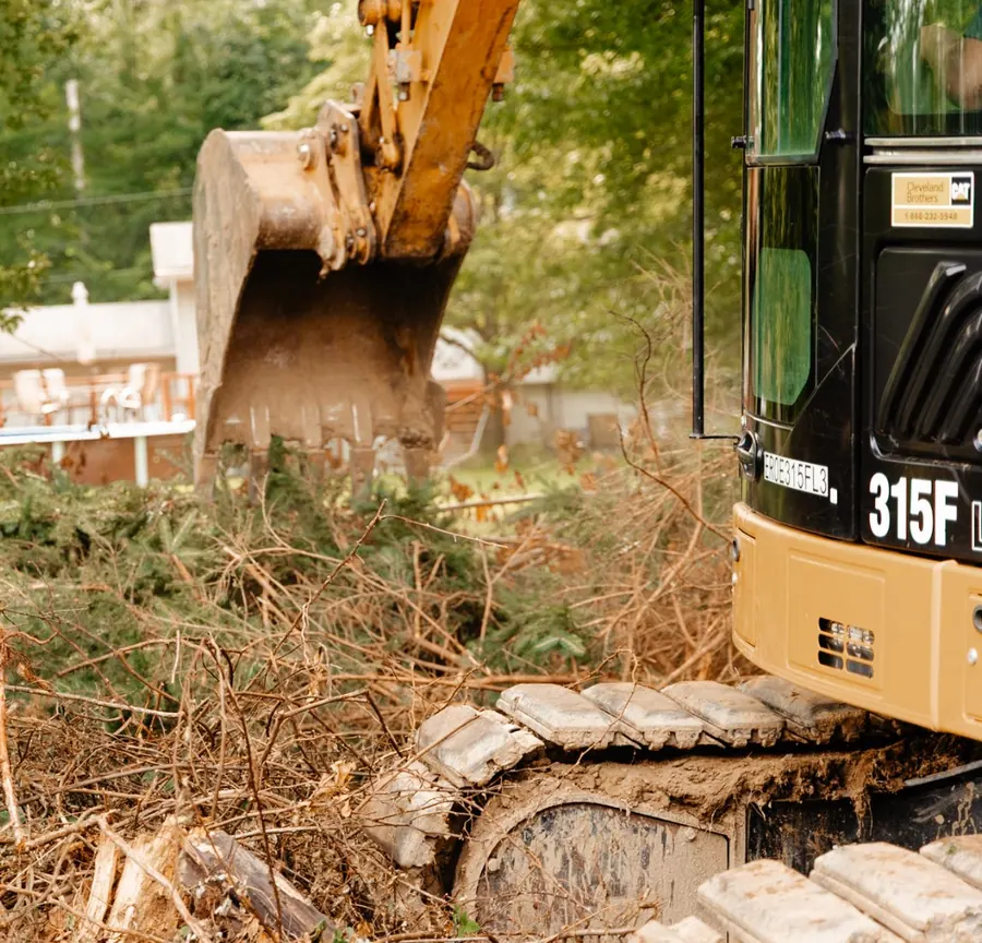 Close view of an excavator track and bucket in a pile of brush