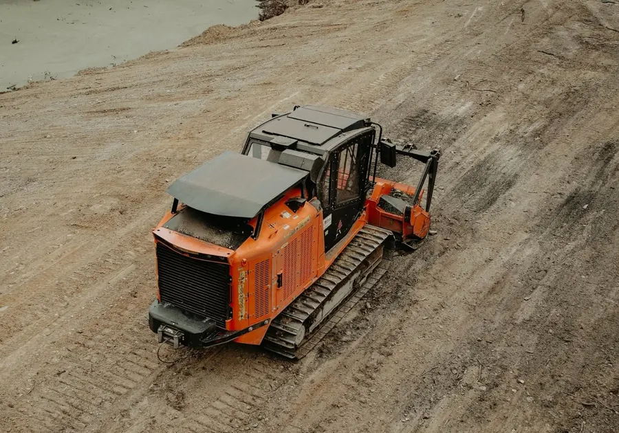 Elevated rear view of a tracked forestry mulcher on a graded dirt slope