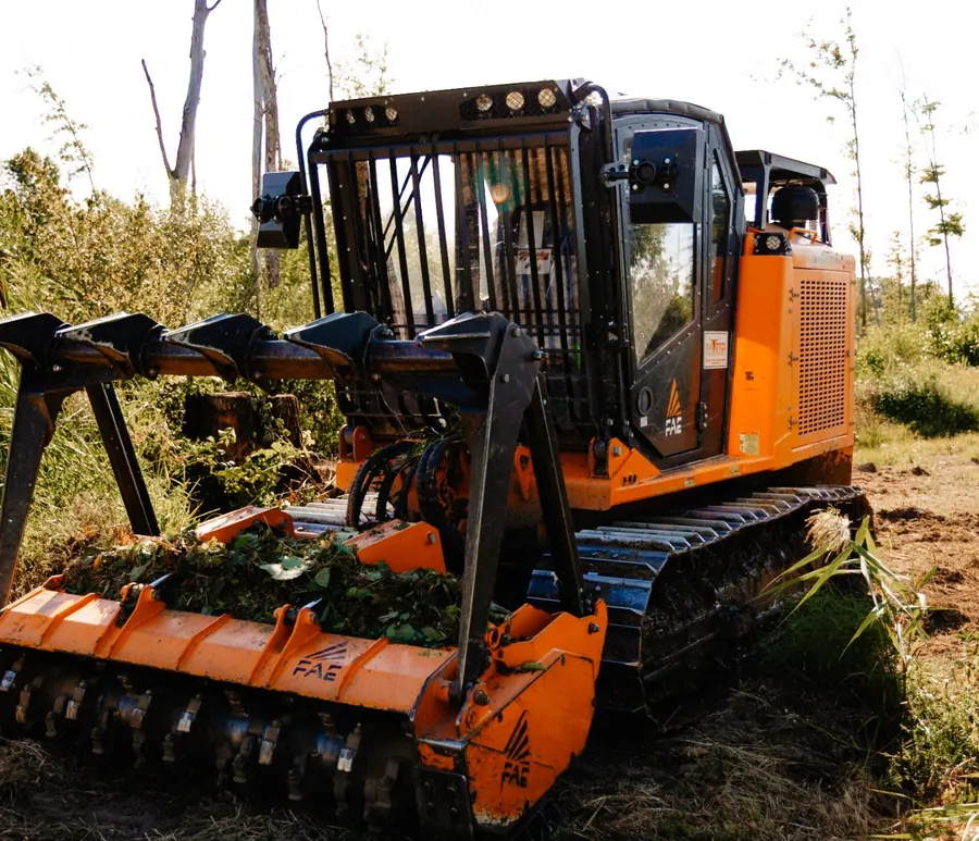 Front view of a tracked forestry mulcher with its mulching head on the ground