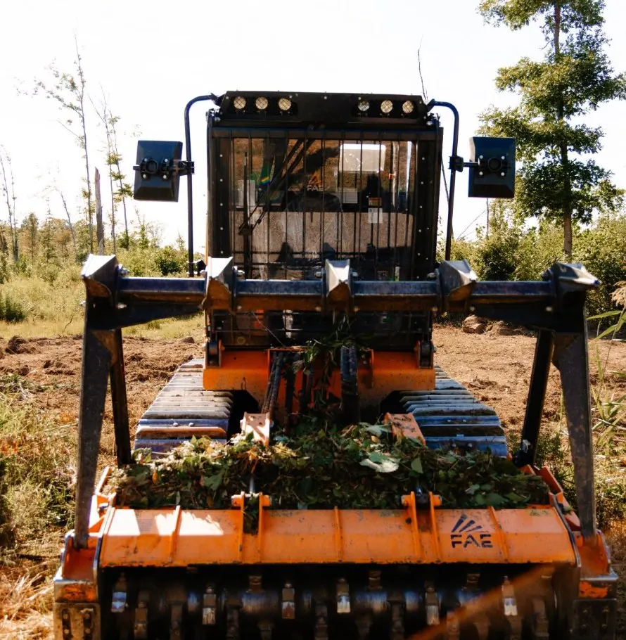 Head-on view of a tracked forestry mulcher with leaves caught on its mulching head
