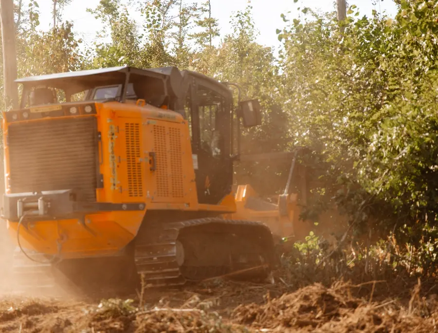 Rear view of a tracked forestry mulcher pushing into dusty brush