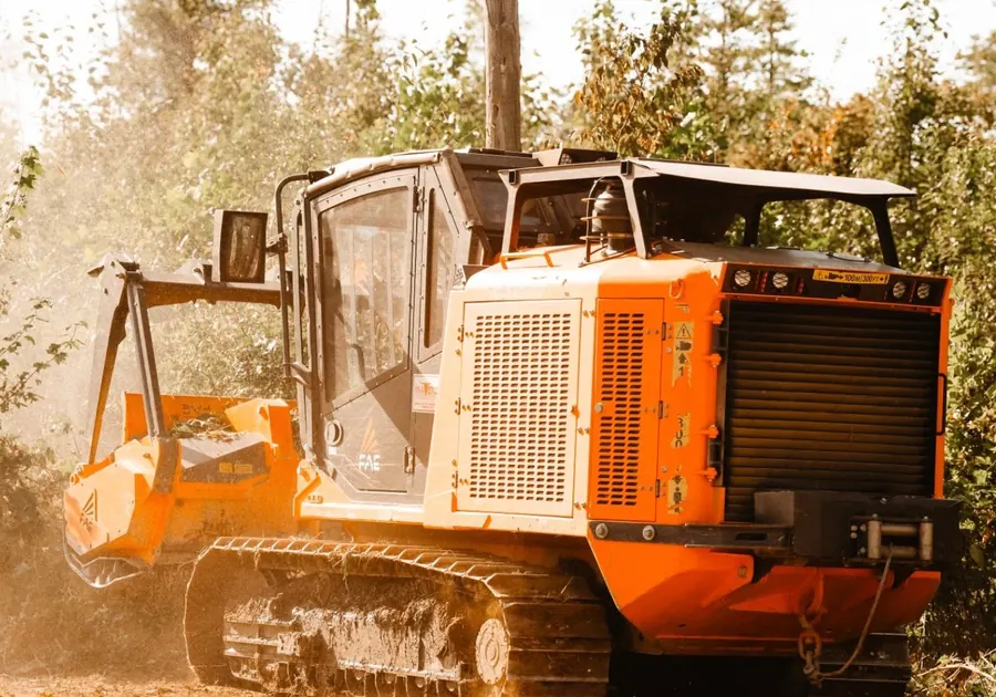 Rear three-quarter view of a tracked forestry mulcher working in dusty brush