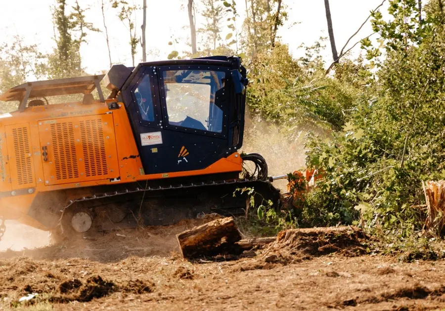 Tracked forestry mulcher pushing into brush with dust and a log in front
