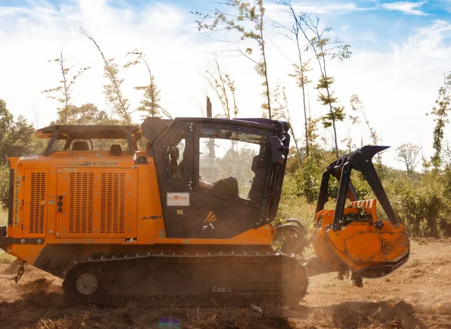 Side profile of a tracked forestry mulcher with its head raised in a clearing