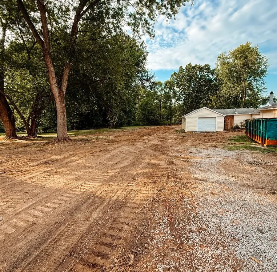 Graded dirt and gravel lane leading to a garage and a dumpster