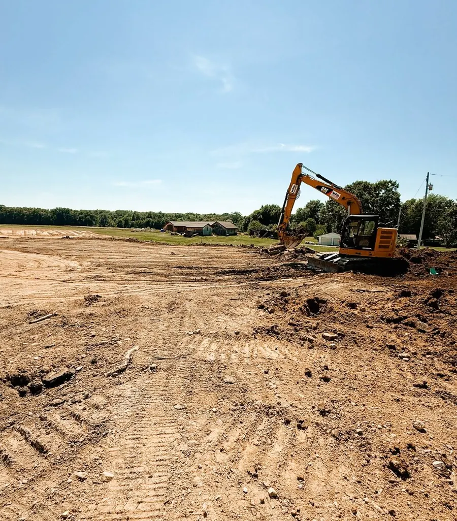 Graded dirt lot with track marks and an excavator working in the distance