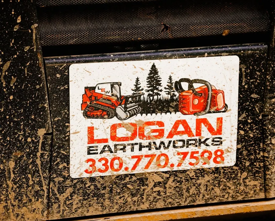 Mud-spattered Logan Earthworks decal with phone number on a machine panel