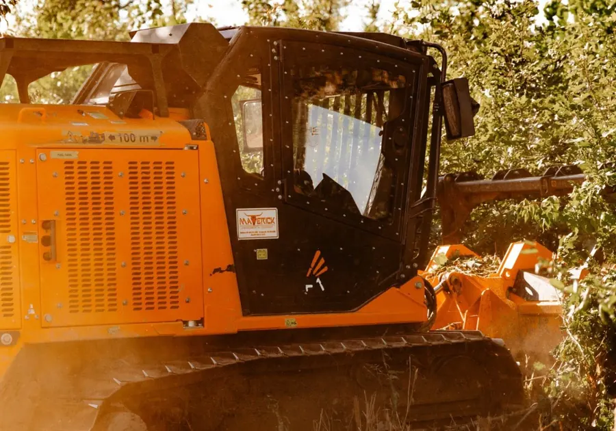 Close view of a forestry mulcher cab and engine panels in sunlit brush