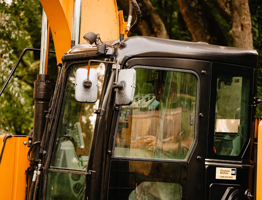 Operator at the controls inside an excavator cab, seen through the glass