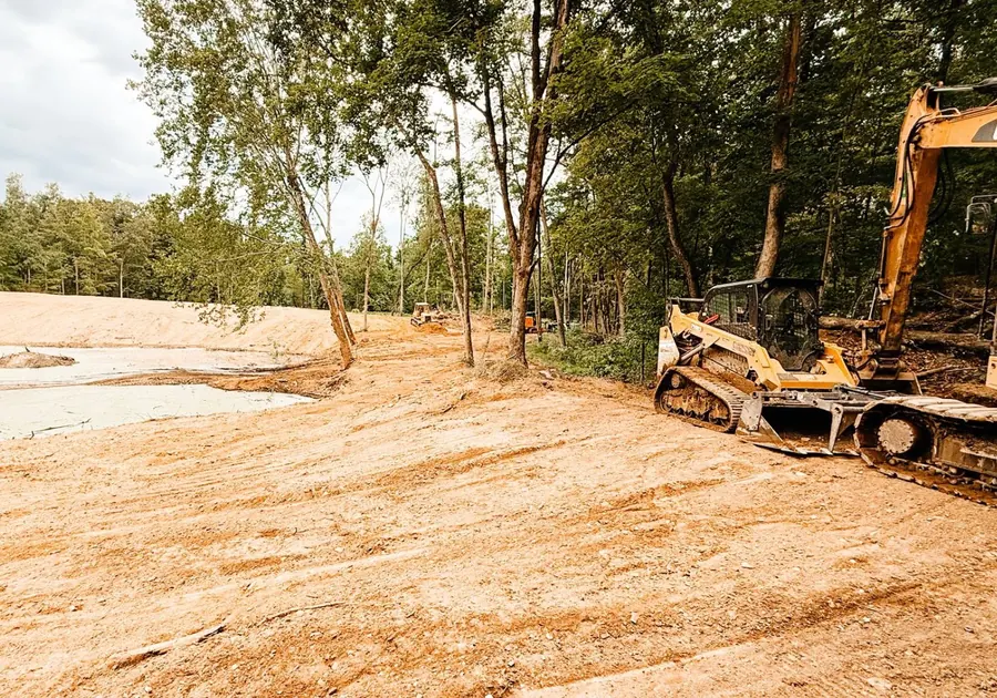 Graded clay pond bank with a compact track loader and excavator parked nearby