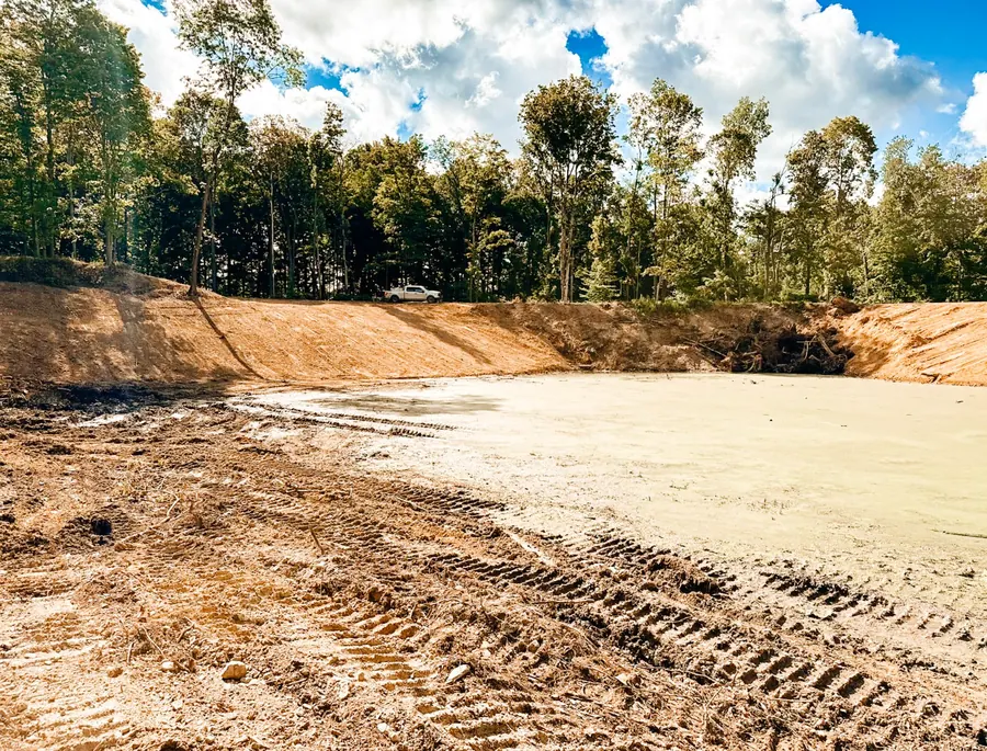 Freshly dug pond with smooth graded clay banks and woods behind