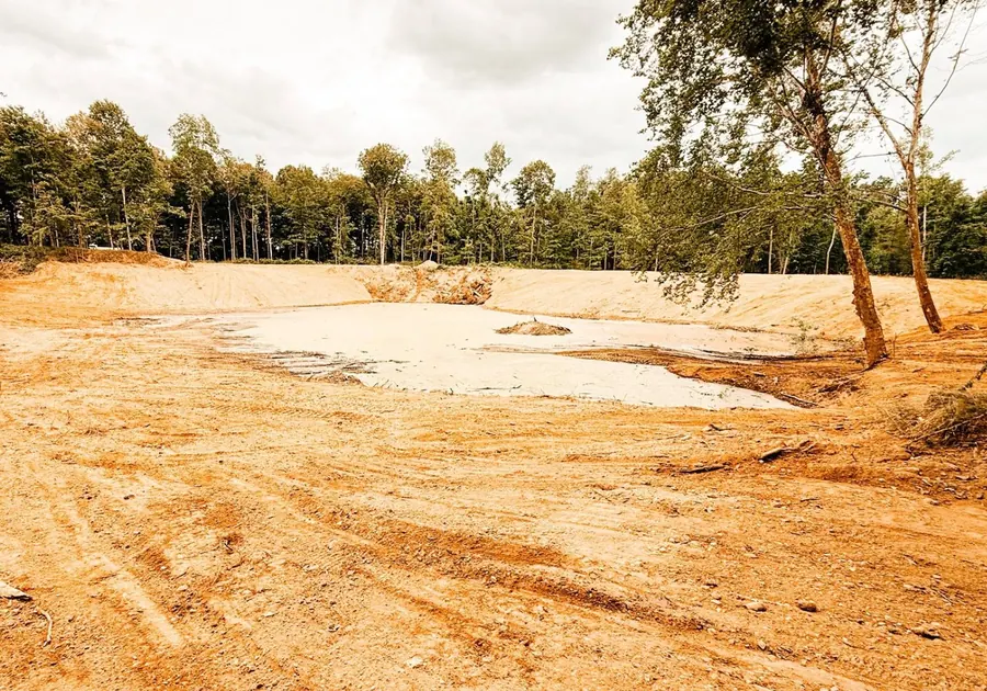 Pond with wide graded clay banks and a wooded shoreline behind