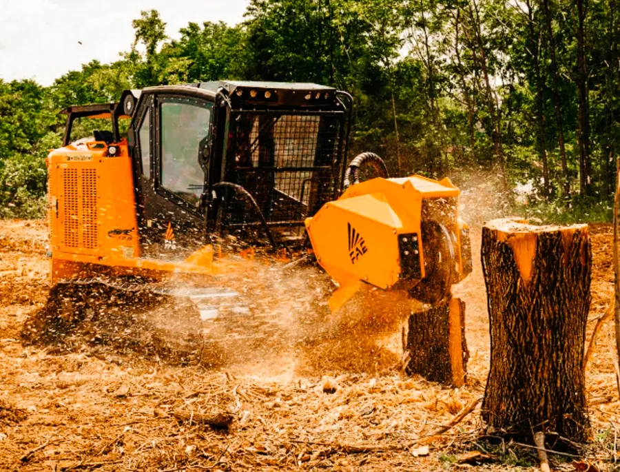 Tracked machine with a stump grinding head throwing chips beside a tall cut stump