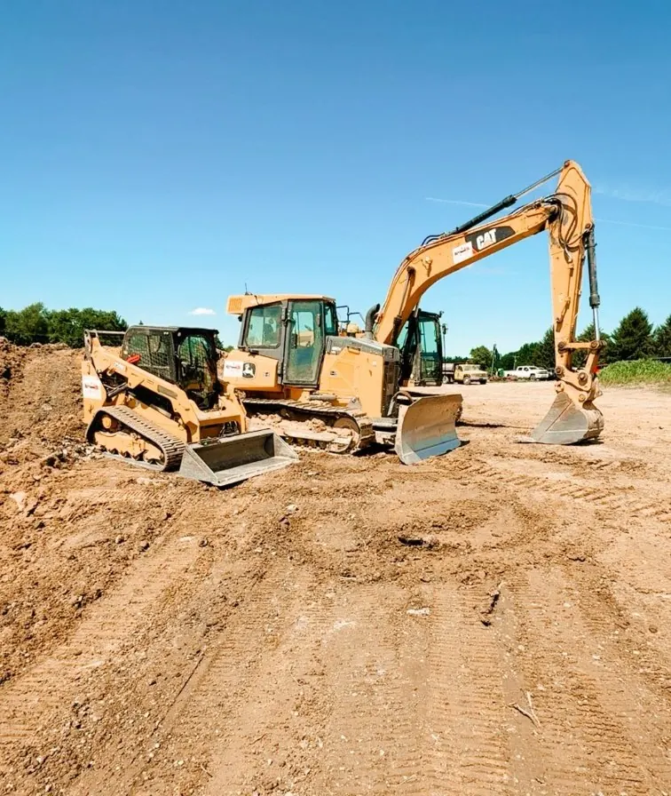 Compact track loader, dozer and CAT excavator lined up on a graded dirt pad