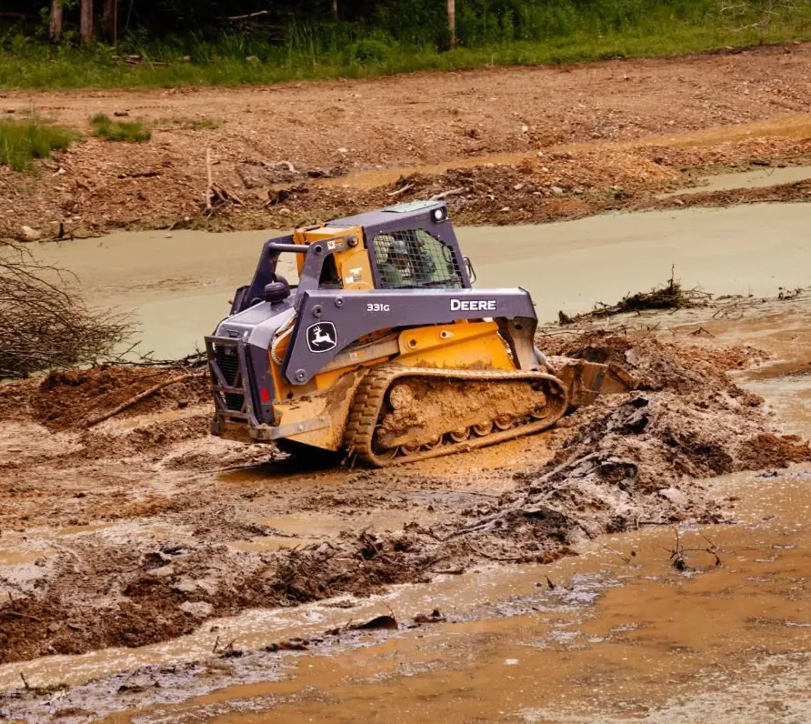 Compact track loader working in deep mud at the edge of a pond